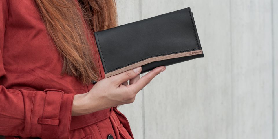 A woman with red hair in an orange coat holding a wallet made of wood and leather Caleo Woman Wallet